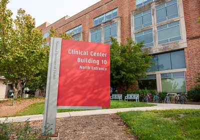 A red sign that reads “Clinical Center, Building 10” outside of a brick building A red sign that reads “Clinical Center, Building 10” outside of a brick building